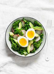 Kale, avocado, radish, cucumbers, olive oil salad and soft boiled egg - delicious healthy breakfast, snack on a light background, top view