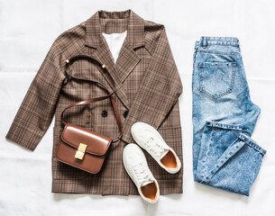 Women's clothing set - plaid jacket, mom's blue jeans, brown crossbody bag and sneakers on a light background, top view