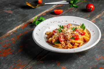 Pasta penne with tomato sauce, chicken meat and tomatoes served with parmesan cheese. Old wood background, top view. Italian cuisine