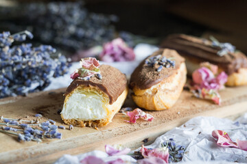 Eclairs with white cream, chocolate topping and dried flowers on cutting board, close-up, selective focus