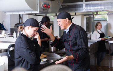 Exasperated head chef scolding upset female employee in kitchen of restaurant..