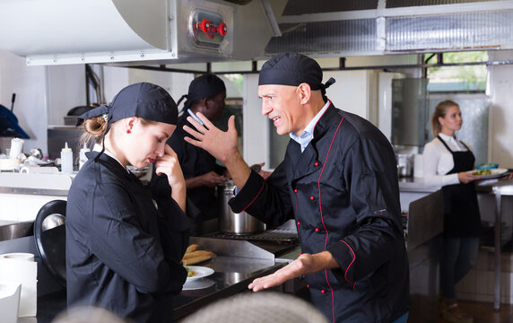 Exasperated head chef scolding upset female employee in kitchen of restaurant.. - Powered by Adobe