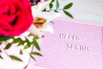 Text Hello Spring on pink letter board and bouquet of colored flowers. Concept Springtime mood and happiness.