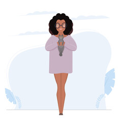 A dark-skinned girl in glasses and a long T-shirt is holding a gray cat. African American girl in full growth. Vector.