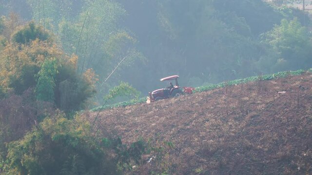 Farmer driving a tractor car in a farm on a hill during morning sunlight.