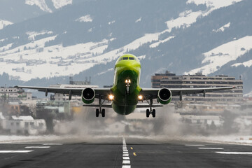 Close up of a green passenger plane speeding on the runway and taking off at Innsbruck airport