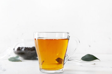 Cup of tea and dry leaves on light background