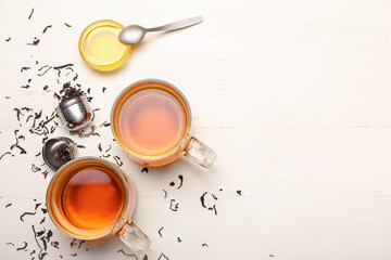 Cups of hot tea, honey and dry leaves on light background