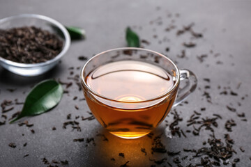 Cup of hot tea and dry leaves on dark background