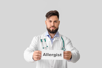 Doctor holding paper with word ALLERGIST on light background