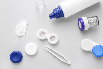 Bottle of solution, tweezers and container with contact lenses on light background