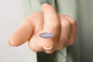 Female hand with contact lens on light background