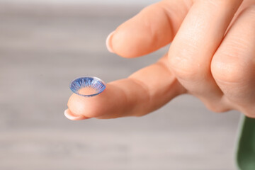 Female hand with contact lens on light background