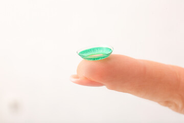 Female finger with contact lens on light background