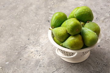 Colander with fresh green figs on grey background