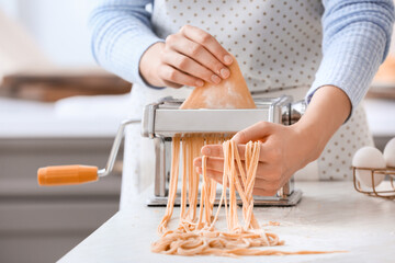 Woman making pasta with machine at table in kitchen - obrazy, fototapety, plakaty