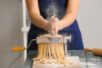 Woman making pasta with machine at table in kitchen
