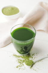 Glass with fresh wheatgrass juice and powder on light background
