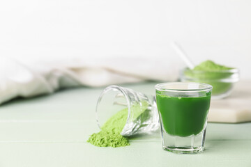 Glass with fresh wheatgrass juice and powder on color wooden background