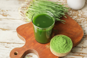 Glass with fresh wheatgrass juice and powder on wooden background