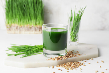 Glass with fresh wheatgrass juice and seeds on light background