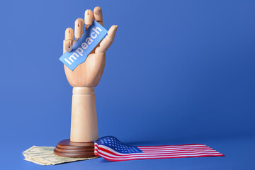 Wooden hand holding paper with word IMPEACH, USA flag and money on color background