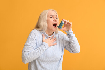 Mature woman with inhaler having asthma attack on color background - obrazy, fototapety, plakaty