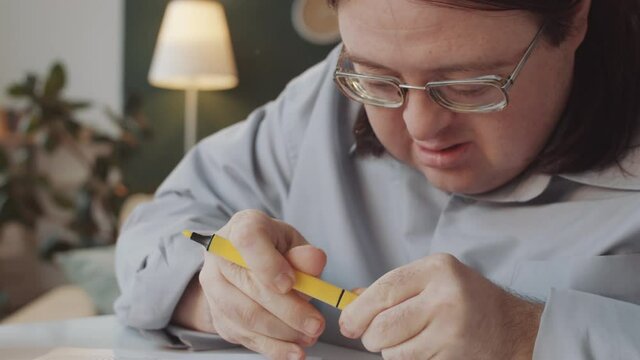 Caucasian man with Down syndrome taking yellow marker pen and drawing inside the lines of patter on coloring page during art therapy at home