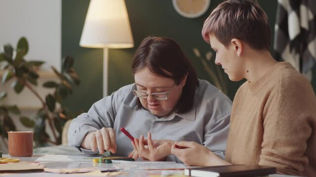 Adult Caucasian man with Down syndrome and female teacher drawing on paper during therapeutic art lesson at home