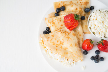 Traditional Russian thin pancakes with cottage cheese and berries in a plate on a white background, top view