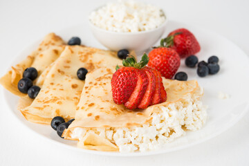 Traditional Russian thin pancakes with cottage cheese and berries in a plate on a white background