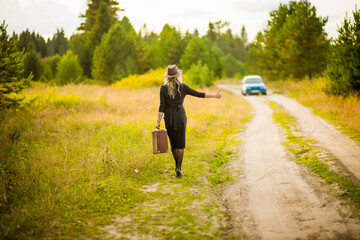 Obraz premium a girl in a black dress and hat walks down the road with a suitcase, selective focus