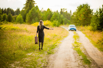 Obraz premium a girl in a black dress and hat walks down the road with a suitcase, selective focus