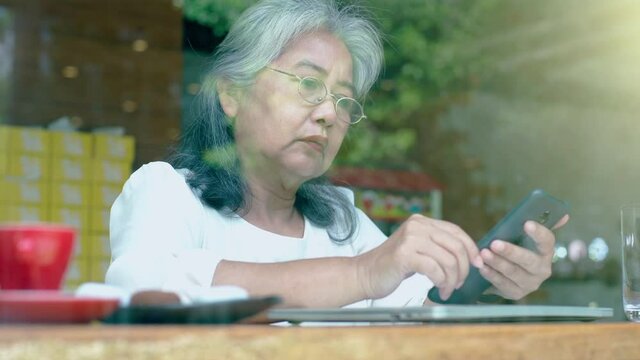 Active senior retired Asian business woman enjoy working on her own online small business and relaxing in a coffeeshop on a bright sunny day