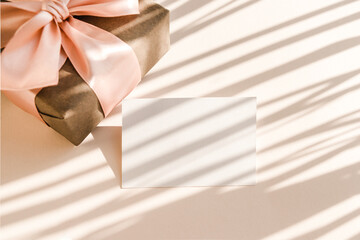 Blank card and gift box on beige background with shadows shape palm leaves. Minimal concept mock up background.
