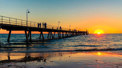 Fototapeta premium Glenelg Beach beach foreshore view with people walking along the pier at sunset, South Australia