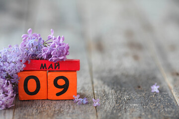Wooden calendar with Russian text May 9 and a bouquet of lilacs on a wooden background. Victory...