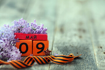 Wooden calendar with Russian text May 9, george ribbon and a bouquet of lilacs on a wooden...