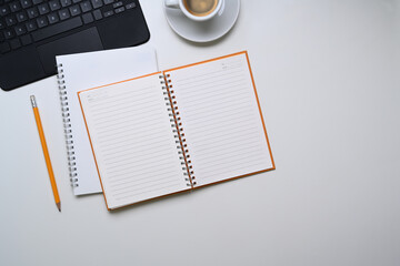 Above view of empty notebook, pencil, coffee cup and copy space on white background.