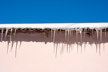Very beautiful icicles hanging from the snow-covered roof. Icicles falling danger concept.