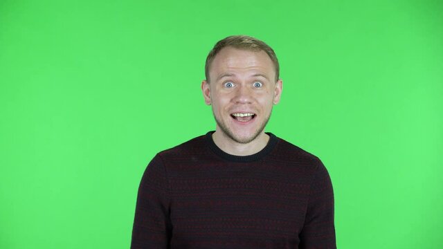 Portrait of a middle aged men saying oh my god with delight and surprised facial expression. Unshaven male in a black red sweater posing on a green screen in the studio. Close up.