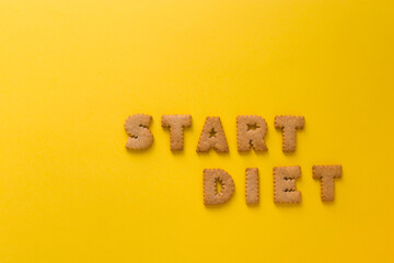 Word Start Diet in the middle of the picture made of tasty crunchy cookies in form of big English alphabet letters, textured bright yellow background, health, dieting and medical concept. Copy space