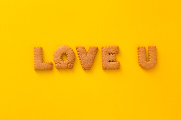 Word Love You U in the middle of the picture made of tasty crunchy cookies in form of big English alphabet letters, textured bright yellow background, health, dieting and medical concept. Copy space