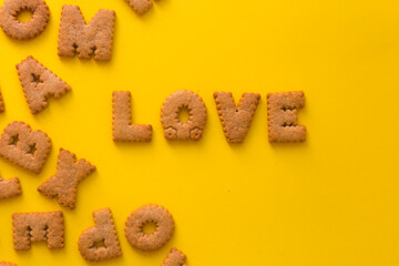 Word Love in the middle of the picture made of tasty crunchy cookies in form of big English alphabet letters, textured bright yellow background, health, dieting and medical concept. Copy space
