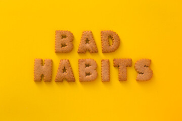 Word Bad Habits in the middle of the picture made of tasty crunchy cookies in form of English big alphabet letters, textured bright yellow background, health, dieting and medical concept. Copy space