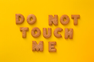 Word Do Not Touch Me in the middle of the picture made of tasty crunchy cookies in form of English alphabet letters, textured bright yellow background, health, dieting and medical concept. Copy space