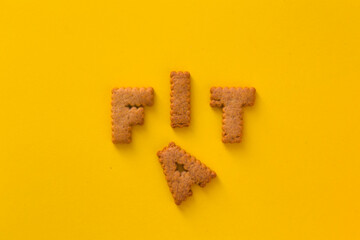 Word Fat Fat in the middle of the picture made of tasty crunchy cookies in form of English big alphabet letters, textured bright yellow background, health, dieting and medical concept. Copy space