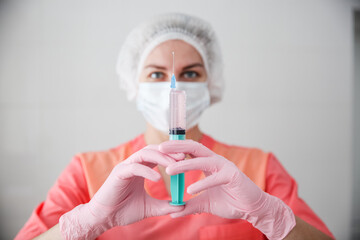 A medical worker in a pink robe, white cap and pink gloves holds a syringe with a vaccine. Coronavirus concept