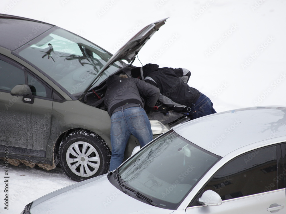 Wall mural two man under the open hood of a car in a snow-covered parking lot, cold engine start and repair on 