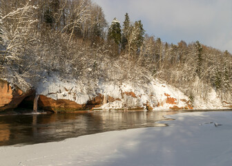 sunny day, blue sky, landscape with red sandstone cliffs that are snow-covered, frozen river, Gauja, Kuku cliffs, Latvia